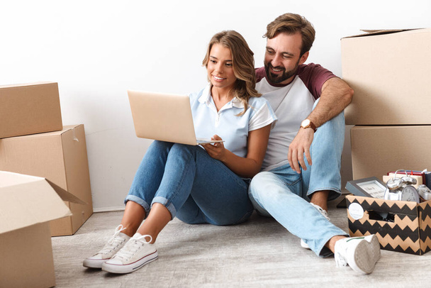 Photo of happy couple using laptop and hugging while sitting - Фото, изображение