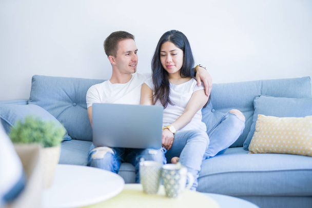 Молода красива пара сидить на дивані, використовуючи ноутбук в новому будинку навколо картонних коробок
 - Фото, зображення