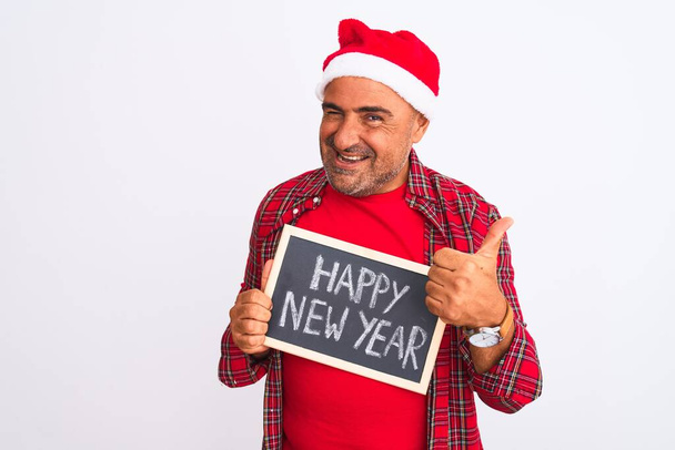 Homme portant le chapeau de Noël Santa tenant tableau noir sur fond blanc isolé heureux avec un grand sourire faisant signe ok, pouce levé avec les doigts, excellent signe
 - Photo, image