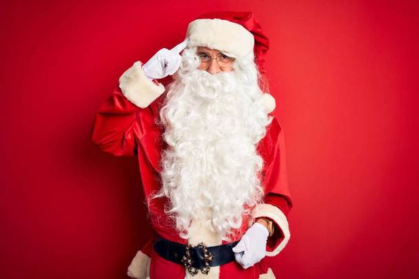 Middelbare leeftijd knappe man dragen Kerstman kostuum staan over geïsoleerde rode achtergrond Lachen wijzen naar het hoofd met een vinger, geweldig idee of gedachte, goed geheugen - Foto, afbeelding