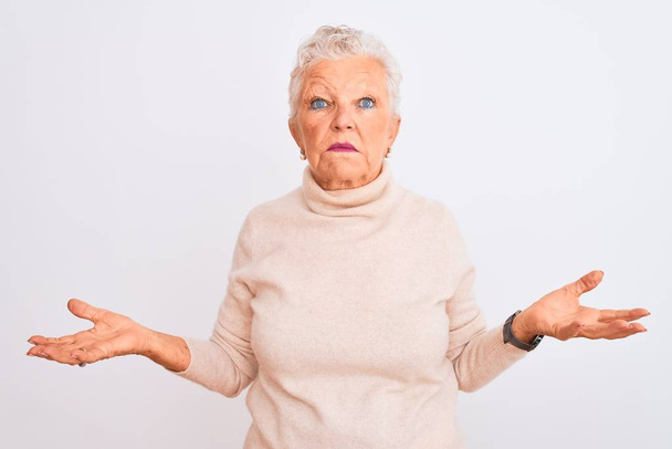 Senior harmaa tukka nainen yllään poolopaita seisoo yli eristetty valkoinen tausta tietämätön ja sekoittaa avosylin, ei aavistustakaan käsite
. - Valokuva, kuva
