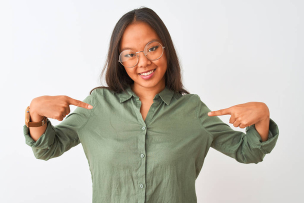 Mladá Číňanka v zelené košili a brýle na izolovaném bílém pozadí vypadá sebevědomě s úsměvem na tváři, ukazuje na sebe s prsty hrdý a šťastný. - Fotografie, Obrázek