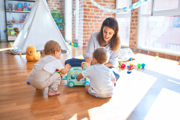 Hermosa maestra y niños pequeños jugando alrededor de un montón de juguetes en el jardín de infantes
 - Foto, imagen
