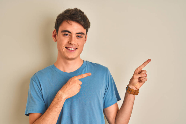 Teenager boy wearing casual t-shirt standing over isolated background smiling and looking at the camera pointing with two hands and fingers to the side. - Photo, Image