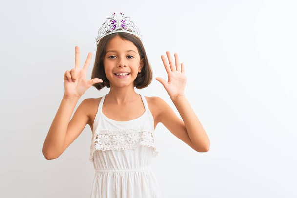 Gyönyörű gyermek lány visel hercegnő korona áll az elszigetelt fehér háttér mutatja, és rámutatva ujjak száma 8 miközben mosolygós magabiztos és boldog. - Fotó, kép
