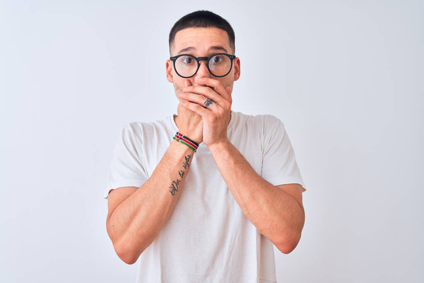 Young handsome man wearing glasses and standing over isolated background shocked covering mouth with hands for mistake. Secret concept. - Fotografie, Obrázek