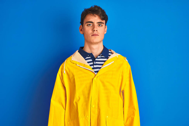 Teenager fisherman boy wearing yellow raincoat over isolated background Relaxed with serious expression on face. Simple and natural looking at the camera. - Fotografie, Obrázek