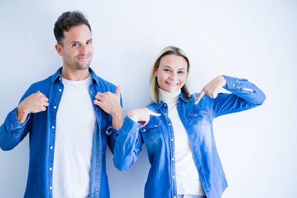 Young beautiful couple wearing denim shirt standing over isolated white background looking confident with smile on face, pointing oneself with fingers proud and happy. - Photo, image