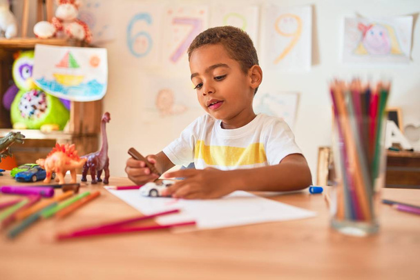 Красивый африканский американец, сидящий в детском саду и рисующий игрушки на автомобиле маркером на столе
 - Фото, изображение