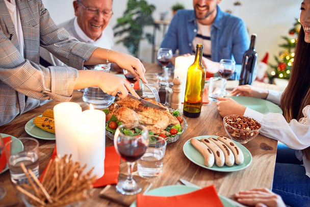 Beautiful family meeting smiling happy and confident. Carving roasted turkey celebrating Christmas at home - Photo, Image