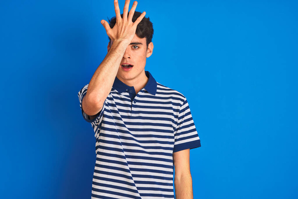 Мальчик-подросток в повседневной футболке, стоящей на синем изолированном фоне, удивленный рукой об голову за ошибкой, помните об ошибке. Забытая, плохая память
. - Фото, изображение