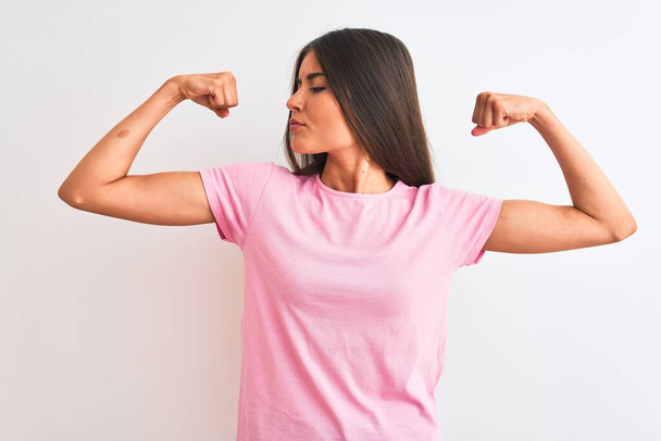 Young beautiful woman wearing pink casual t-shirt standing over isolated white background showing arms muscles smiling proud. Fitness concept. - Foto, Bild