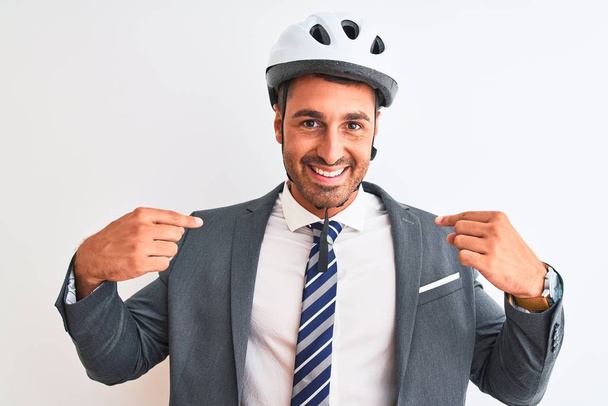 Młody przystojny biznesmen w garniturze, krawacie i kasku rowerowym na odosobnionym tle wyglądający pewnie z uśmiechem na twarzy, wytykający się palcami dumną i szczęśliwą. - Zdjęcie, obraz