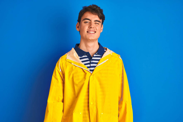 Teenager fisherman boy wearing yellow raincoat over isolated background winking looking at the camera with sexy expression, cheerful and happy face. - Fotografie, Obrázek