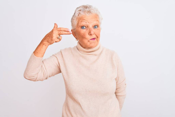 Femme âgée aux cheveux gris portant un pull à col roulé debout sur un fond blanc isolé Tir et se suicider en se pointant la main et les doigts vers la tête comme une arme à feu, geste de suicide
. - Photo, image