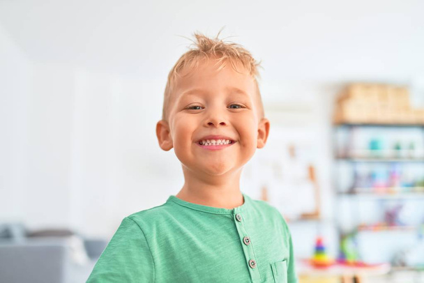 Adorable niño rubio sonriendo feliz. De pie jugando alrededor de un montón de juguetes en el jardín de infancia
 - Foto, imagen