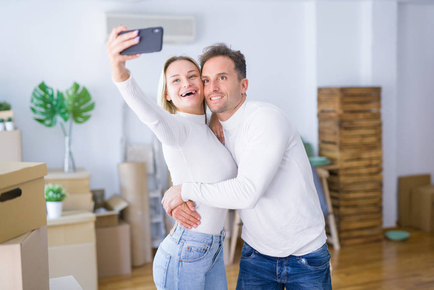 Jeune beau couple debout en utilisant un smartphone pour prendre selfie à la nouvelle maison autour des boîtes en carton
 - Photo, image