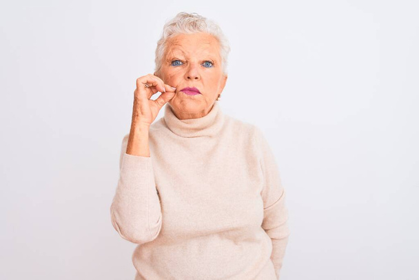 Senior grey-haired woman wearing turtleneck sweater standing over isolated white background mouth and lips shut as zip with fingers. Secret and silent, taboo talking - Foto, imagen