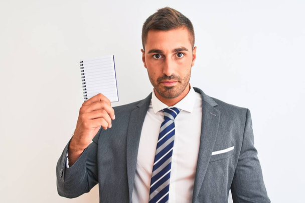 Young handsome business man holding blank notebook over isolated background with a confident expression on smart face thinking serious - Foto, Imagen