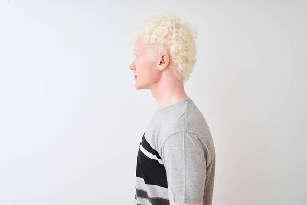 Молодий альбіно блондин в повсякденній футболці стоїть над ізольованим білим тлом, дивлячись в бік, розслабляє профільну позу з природним обличчям з впевненою посмішкою
. - Фото, зображення