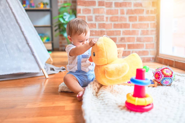 Beautiful toddler sitting on the blanket playing with duck doll at kindergarten - Photo, Image