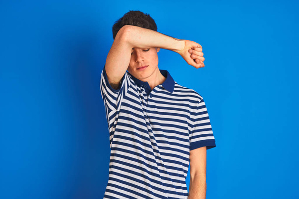 Teenager boy wearing casual t-shirt standing over blue isolated background covering eyes with arm, looking serious and sad. Sightless, hiding and rejection concept - Fotó, kép