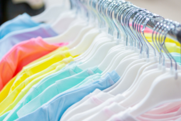 Desenfoque fondo fondo fondo fondo bokeh, ropa de verano colgando de perchas en una tienda. algodón natural camisetas blanco rosa verde azul
. - Foto, imagen