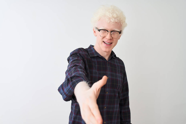 Jonge albino blonde man draagt casual shirt en bril over geïsoleerde witte achtergrond glimlachend vriendelijk aanbieden van handdruk als groet en gastvrij. Succesvolle bedrijfsvoering. - Foto, afbeelding