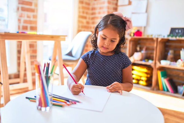 Όμορφο κοριτσάκι ζωγραφίζει χαριτωμένο σχέδιο χρησιμοποιώντας χρωματιστά μολύβια στο νηπιαγωγείο - Φωτογραφία, εικόνα