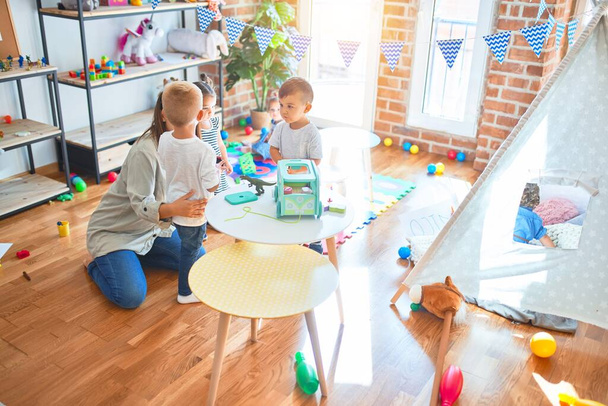 Belle enseignante et groupe de tout-petits jouant autour de beaucoup de jouets à la maternelle
 - Photo, image
