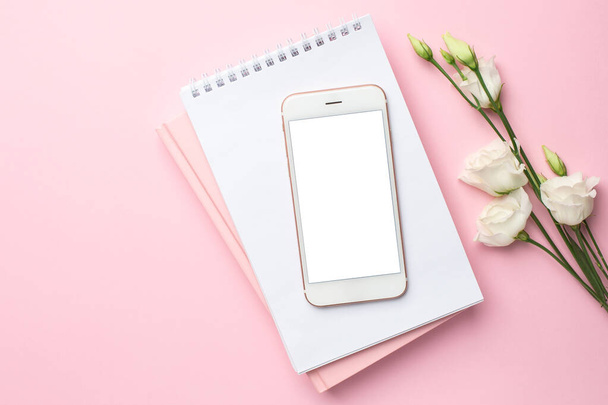 Mobile phone, white eustoma flower and notebook on pink background. Women's business technology composition - Фото, изображение