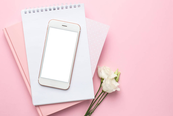 Mobile phone, white eustoma flower and notebook on pink background. Women's business technology composition - Foto, imagen