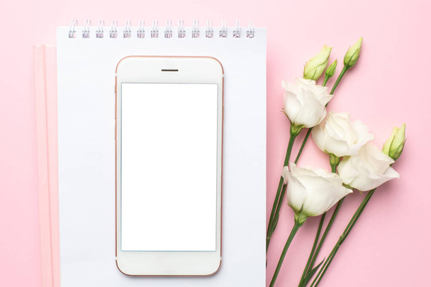Mobile phone, white eustoma flower and notebook on pink background.Women's business technology composition - Foto, Bild