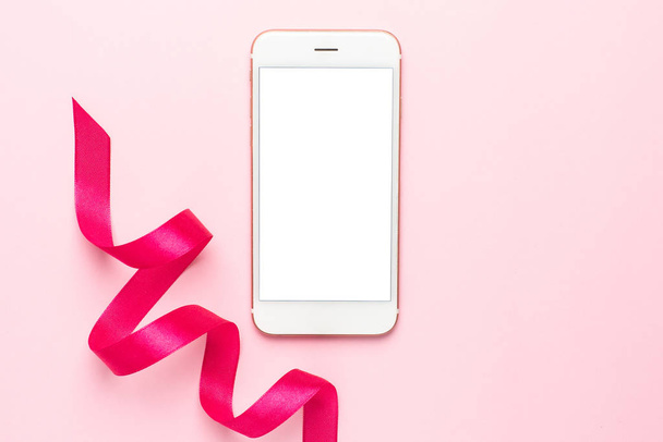 Mobile phone and gift ribbon on pink background. - Foto, Bild