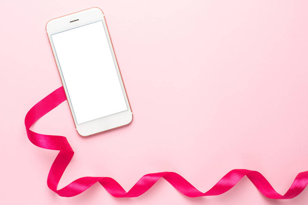 Mobile phone and gift ribbon on pink background. - Valokuva, kuva