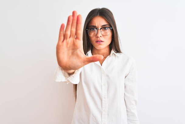 Young beautiful businesswoman wearing glasses standing over isolated white background doing stop sing with palm of the hand. Warning expression with negative and serious gesture on the face. - Photo, Image