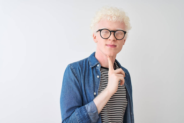 junger albinoblonder Mann mit Jeanshemd und Brille über isoliertem weißem Hintergrund, der konzentriert mit dem Finger am Kinn über Zweifel nachdenkt und fragend aufblickt - Foto, Bild