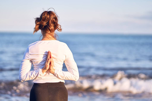 Joven hermosa deportista practicando yoga. Entrenador de pie en bakcview enseñanza oración inversa pose en la playa
 - Foto, Imagen