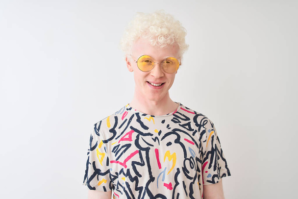 Young albino blond man wearing colorful t-shirt and sunglasses over isolated red background with a happy and cool smile on face. Lucky person. - Foto, imagen