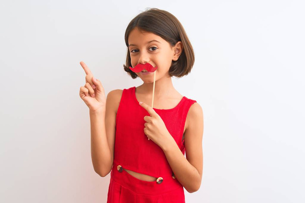 Beautiful child girl holding fanny party mustache standing over isolated white background very happy pointing with hand and finger to the side - Photo, Image