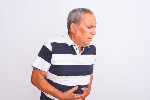 Senior grey-haired man wearing casual striped polo standing over isolated white background with hand on stomach because indigestion, painful illness feeling unwell. Ache concept. - Photo, Image