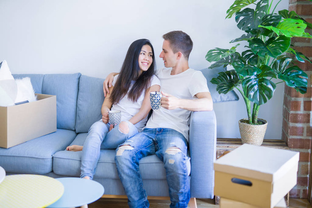 Nuori kaunis pari istuu sohvalla juomassa kahvia uudessa kodissa pahvilaatikoiden ympärillä.
 - Valokuva, kuva