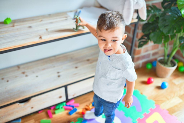 Adorable niño sonriendo feliz. De pie jugando alrededor de un montón de juguetes en el jardín de infancia
 - Foto, imagen