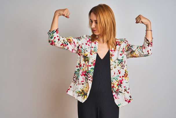 Jonge Kaukasische zakenvrouw dragen voorjaar bloemenjasje pak over geïsoleerde achtergrond tonen armen spieren glimlachen trots. Fitness concept. - Foto, afbeelding