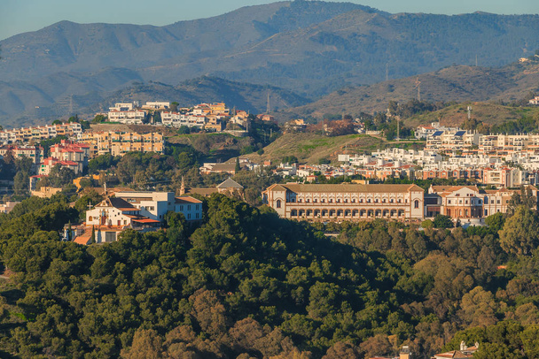 Πανοραμική θέα στη Μάλαγα από το λόφο της περιοχής Barcenillas με Sagrada Familia El Monte. Λόφοι με δάση, δέντρα και πολυκατοικίες σε μια ηλιόλουστη μέρα. Πανεπιστήμιο με κτίρια - Φωτογραφία, εικόνα