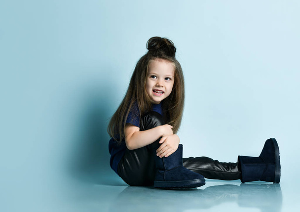Small smiling girl model with long hair in stylish casual clothing and ugg boots sitting on floor - Фото, изображение