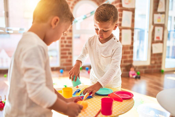 Adoráveis gêmeos loiros brincando em torno de lotes de brinquedos. Cozinhar brinquedo de comida de plástico no jardim de infância
 - Foto, Imagem