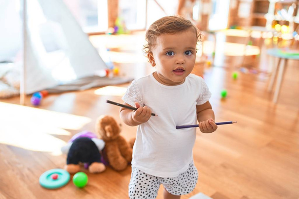 Adorable niño sosteniendo lápices de pie alrededor de un montón de juguetes en el jardín de infantes
 - Foto, imagen