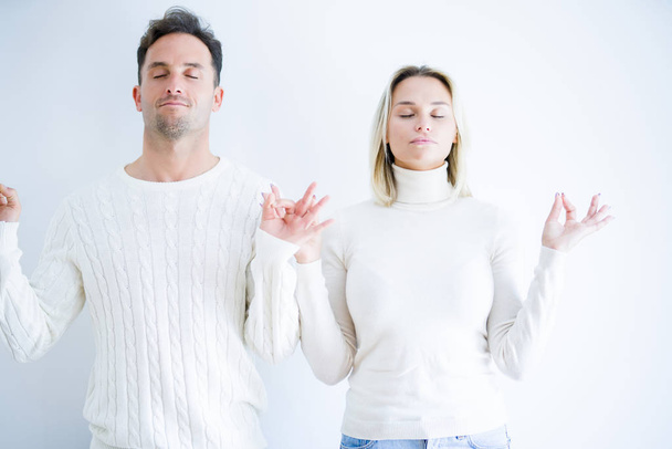 Young beautiful couple wearing casual t-shirt standing over isolated white background relax and smiling with eyes closed doing meditation gesture with fingers. Yoga concept. - Photo, Image