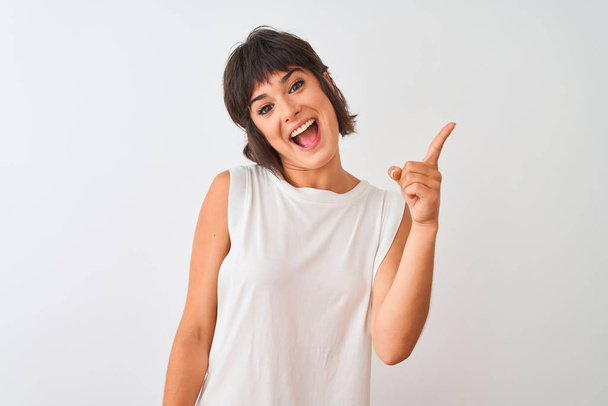 Молодая красивая женщина в повседневной футболке стоит на изолированном белом фоне, показывая пальцем вверх с успешной идеей. Взволнован и счастлив. Номер один
. - Фото, изображение